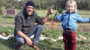 Dad and son holding a carrot by the top leaves.